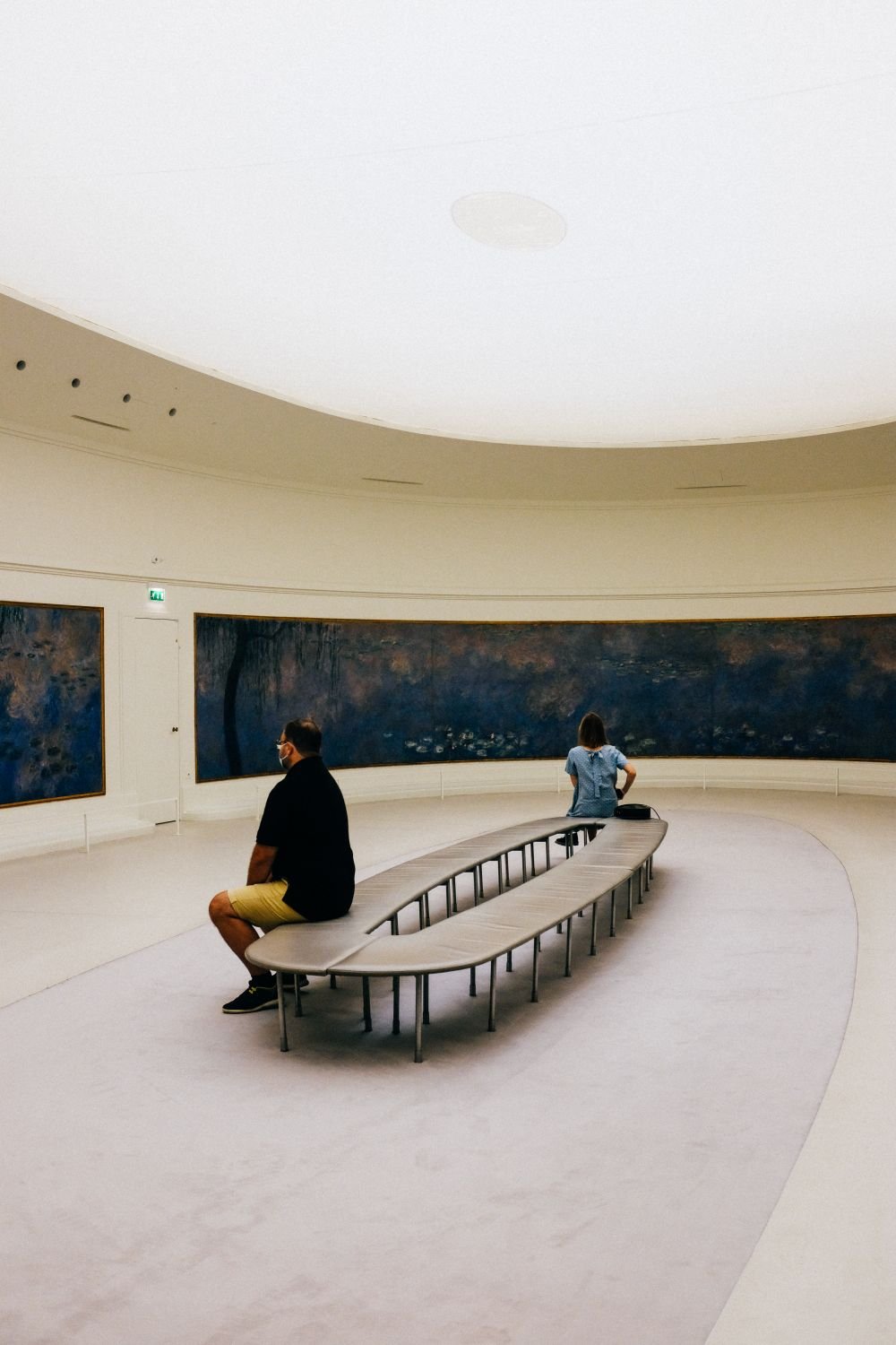 Round gallery with a glass ceiling and visitors seated on a curved bench