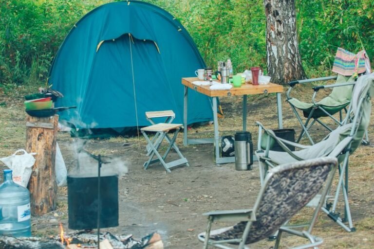 Tent with camping chairs and a campfire among green trees