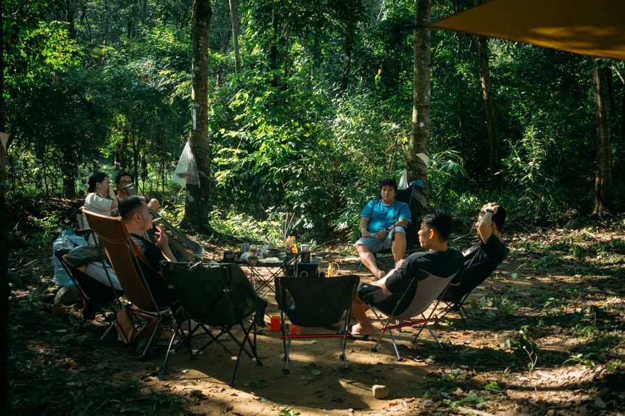 Group of friends relaxing at a sunlit forest campsite