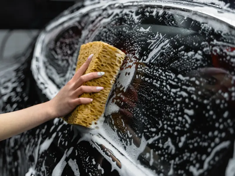 Hand scrubbing a car with a soapy sponge