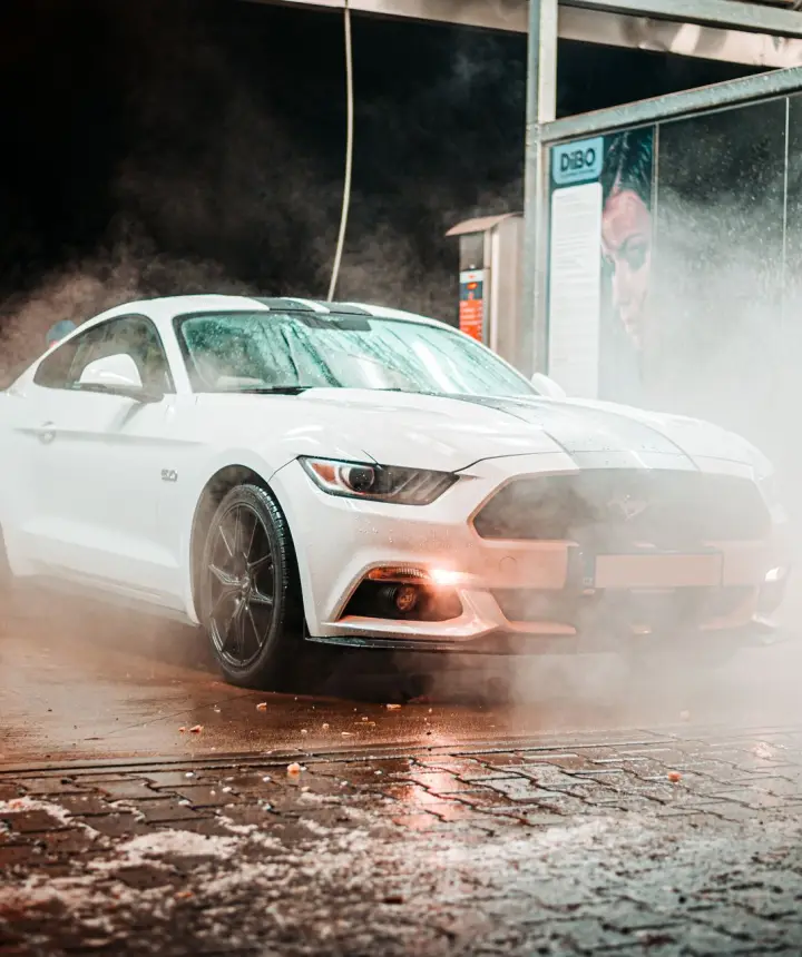 White sports car in a cloud of steam inside a car wash bay