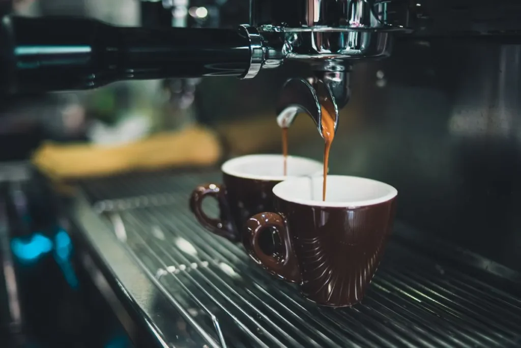 Espresso pouring from a portafilter into two brown cups