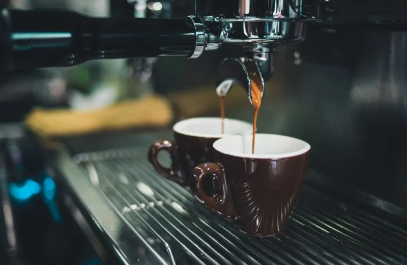 Espresso pouring from a portafilter into two brown cups