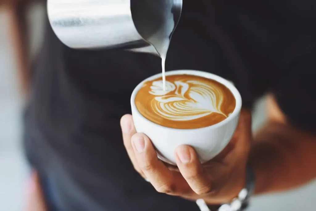 Barista pouring steamed milk into a cappuccino to make latte art