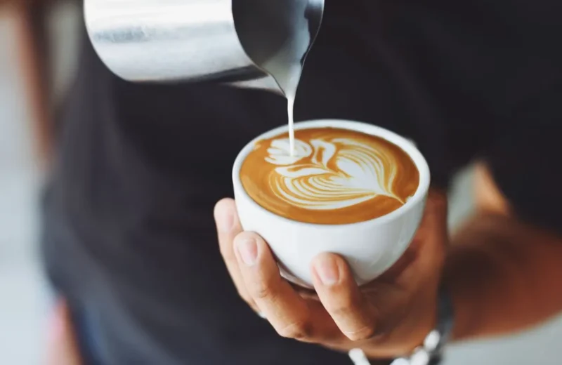 Barista pouring steamed milk into a cappuccino to make latte art