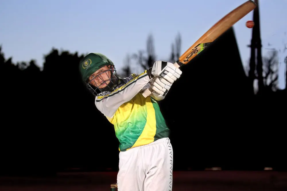 Cricketer in a green and yellow kit swinging the bat