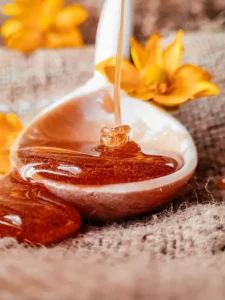 Honey dripping from a spoon with yellow flowers