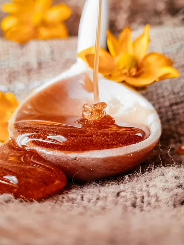 Honey dripping from a spoon with yellow flowers