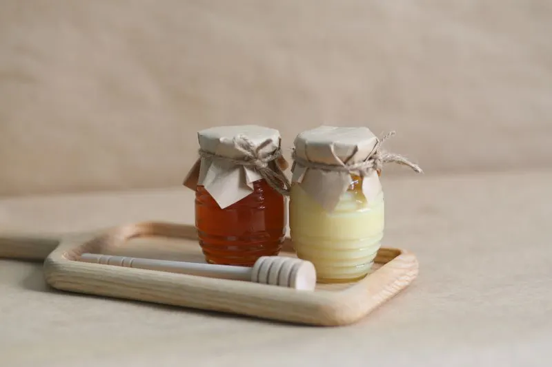 Two honey jars on a wooden tray with dipper
