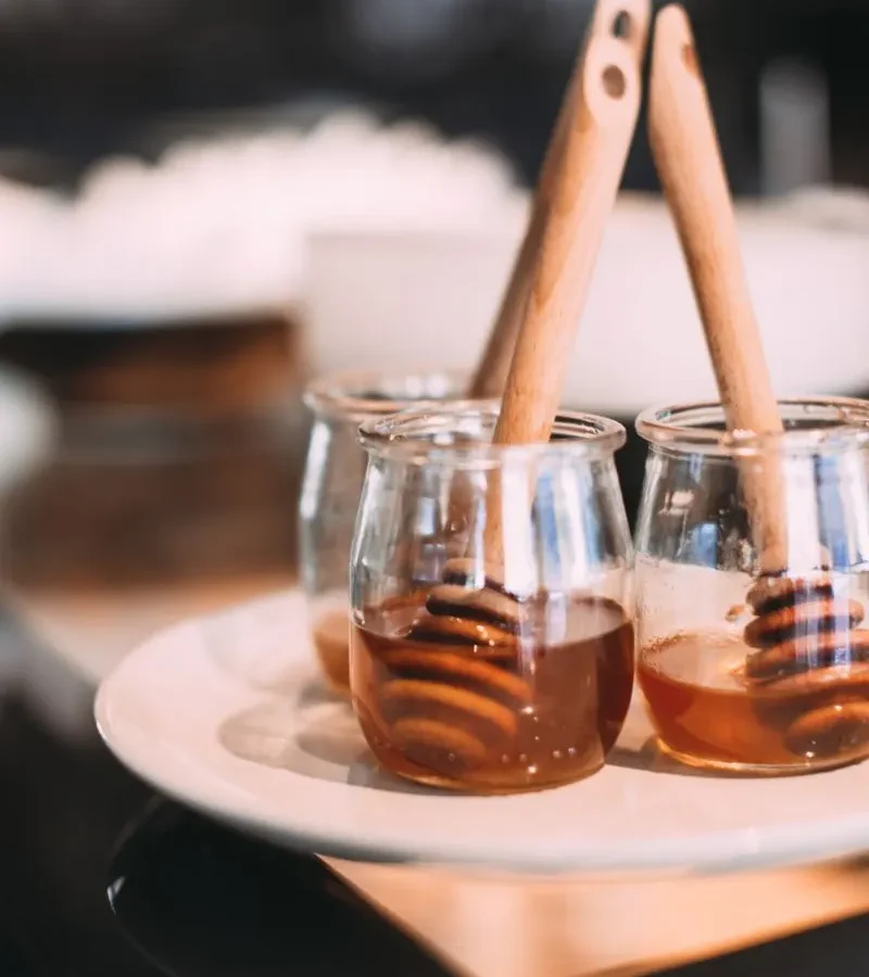 Three glass jars of honey with wooden dippers