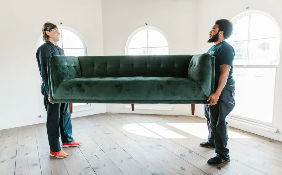 Two movers lifting a green sofa