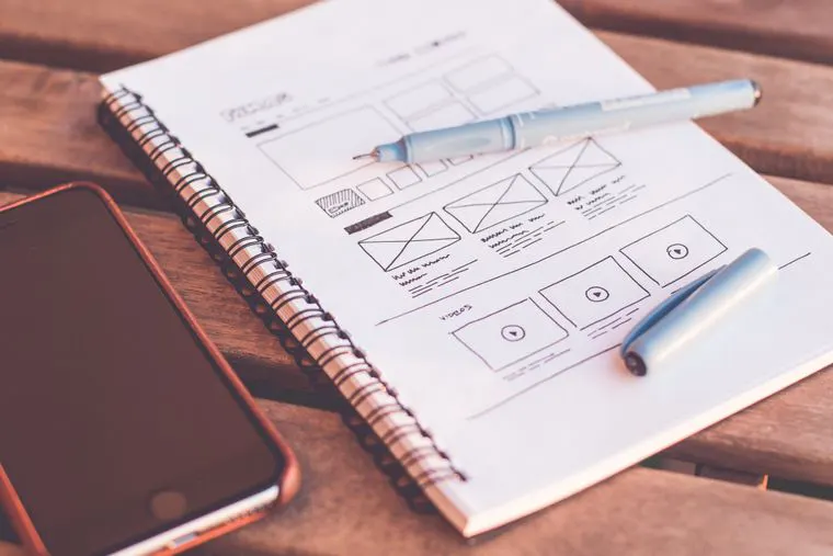 Designer sketching app wireframes beside a laptop