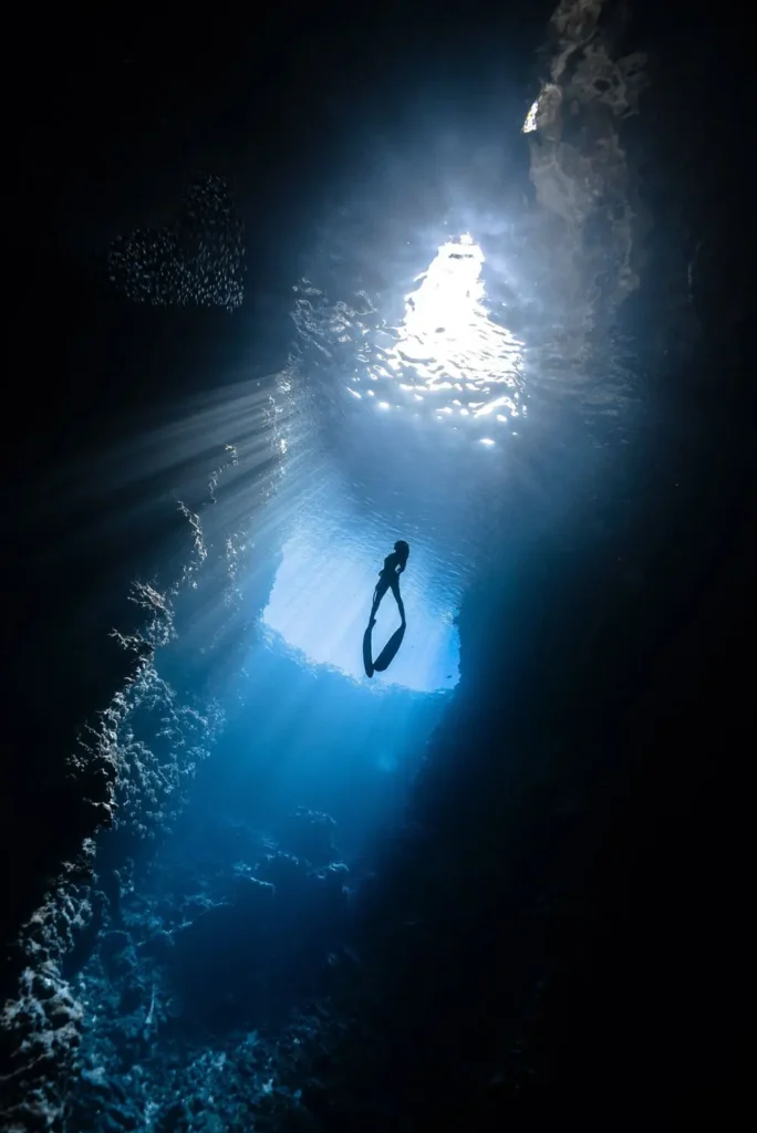 Diver silhouetted inside a sunlit underwater cavern