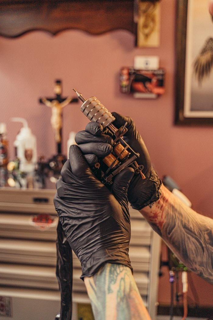 Gloved hand holding a coil tattoo machine