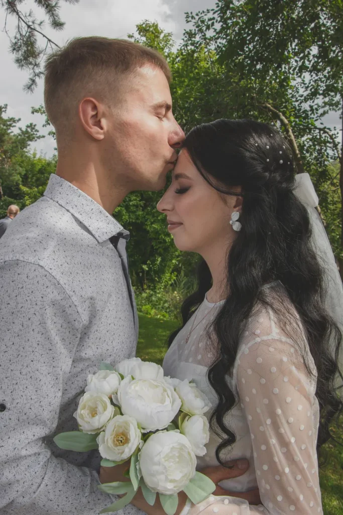Groom kissing the bride's forehead outdoors