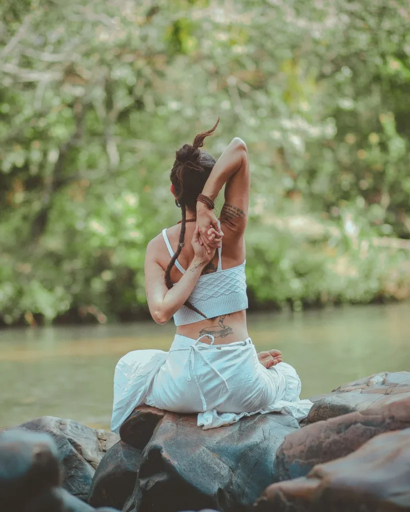 Woman in a seated pose beside a calm river