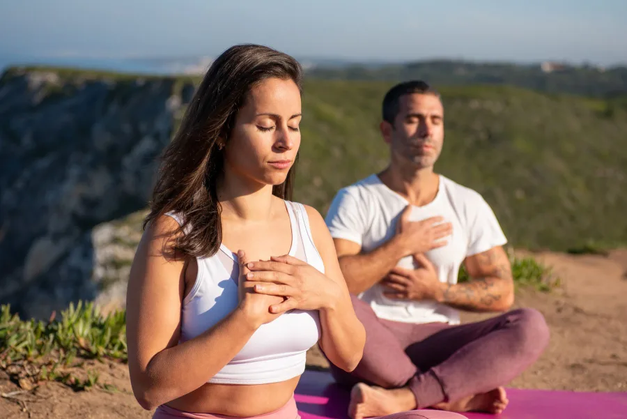 Two people meditating on a green hillside