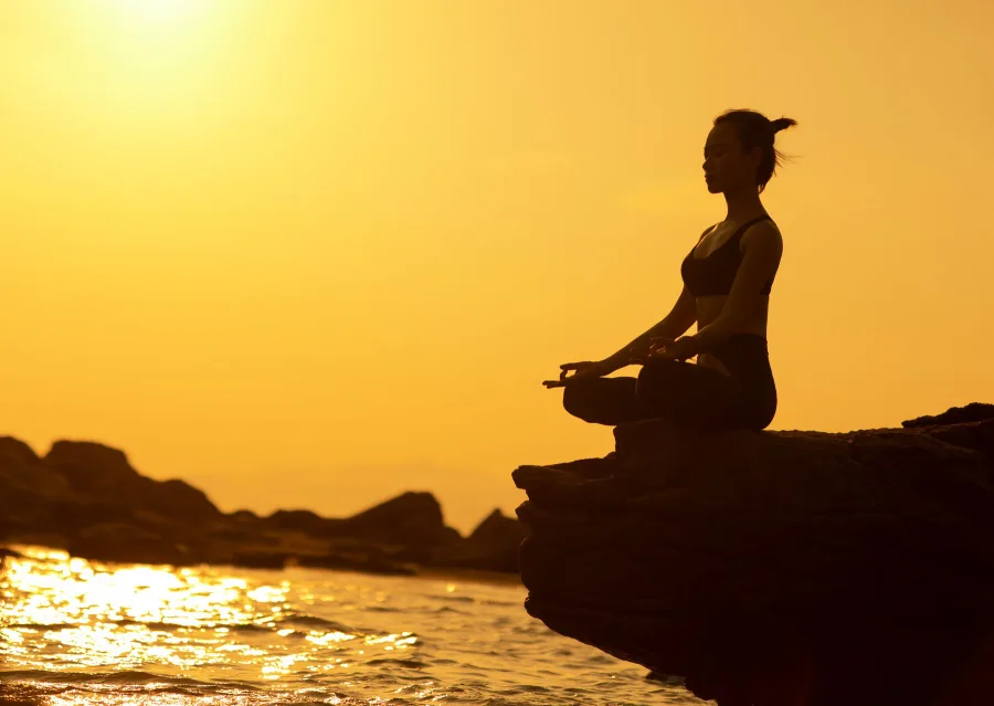 Woman in lotus pose on a cliff above the sea